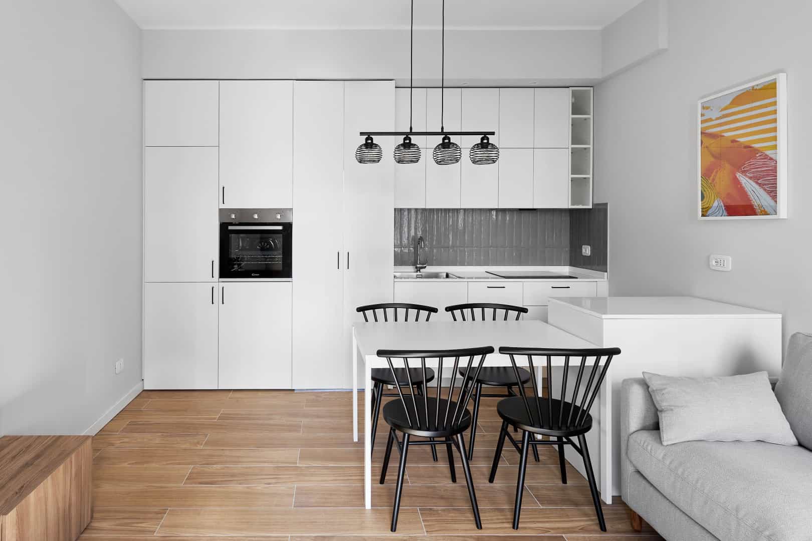 Modern white kitchen with black dining chairs and wooden flooring.