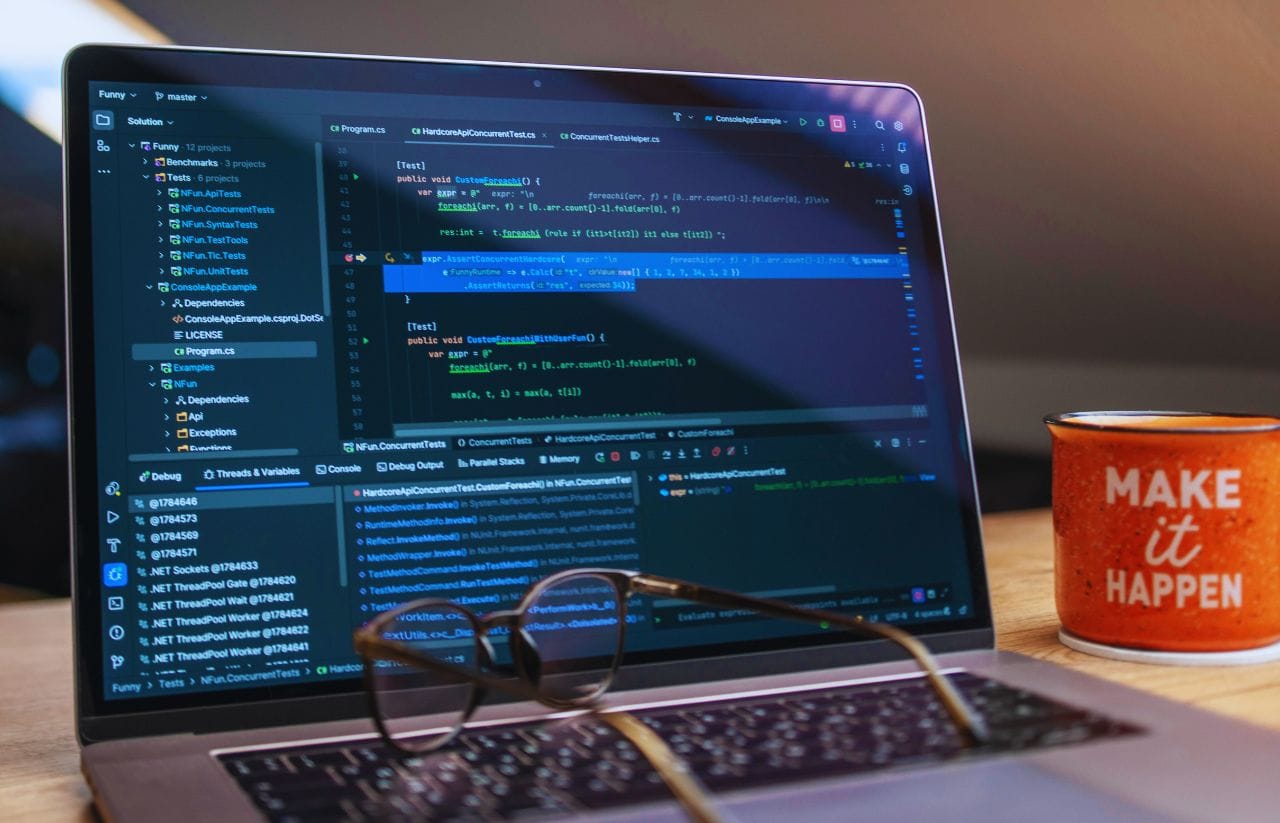 Laptop showing a blue-themed code editor with glasses resting on the keyboard and a red mug that says 'MAKE it HAPPEN' on the desk.