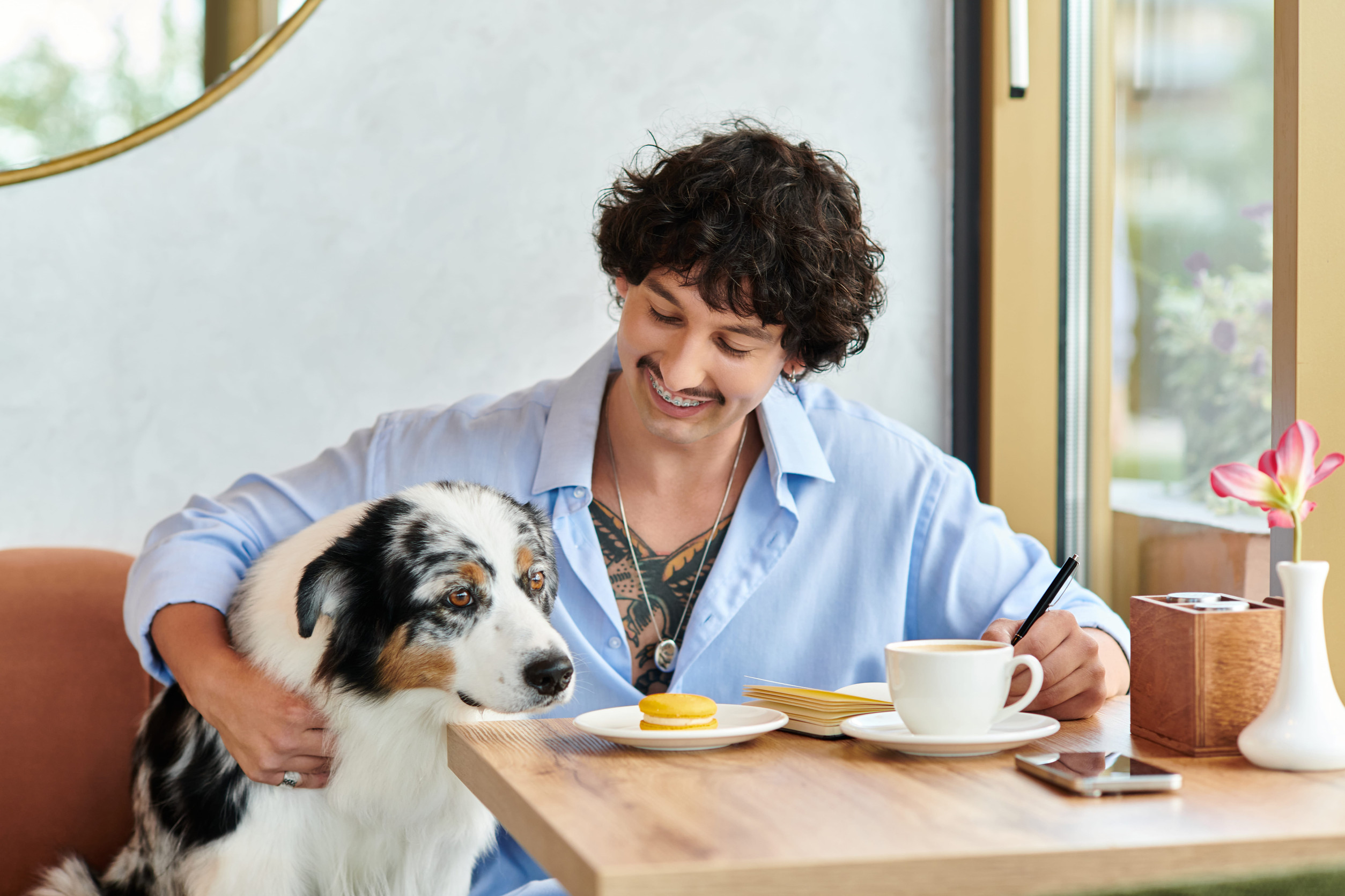 Woman with braces smiles while petting a white and black dog at a cafe table.