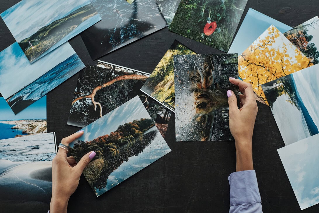 Top-down view of two hands arranging scattered nature photos on a dark table surface.