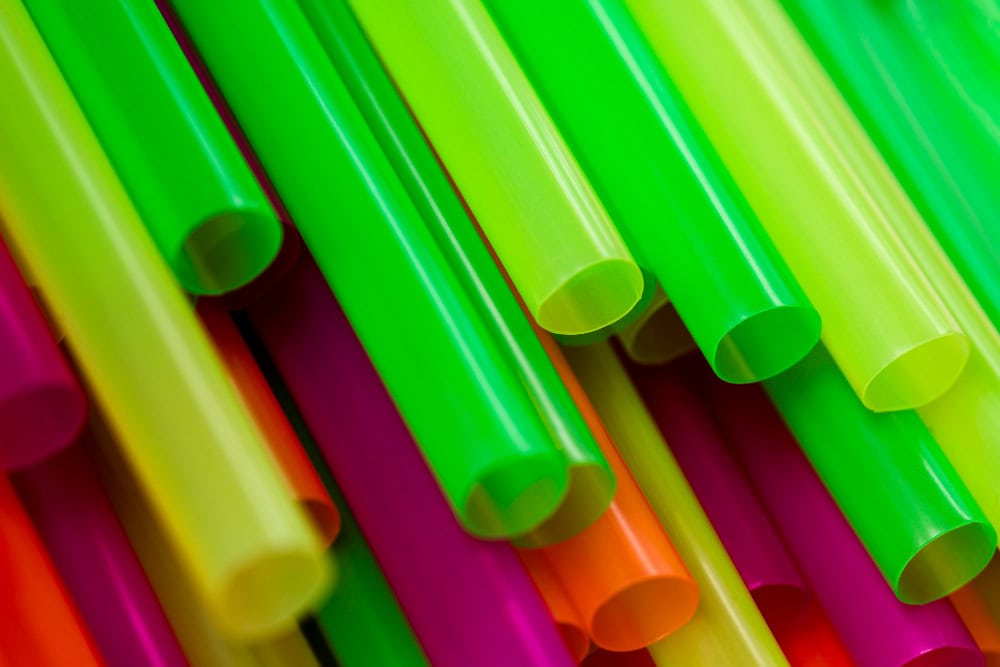 Close-up of neon-colored plastic drinking straws in green, yellow, orange, and pink.