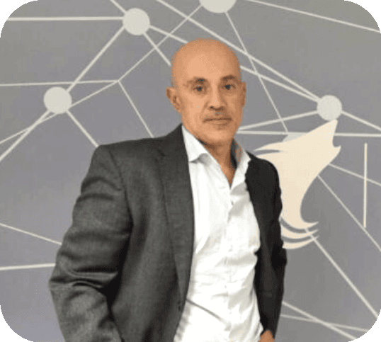 Portrait of a bald man in a gray suit standing with one hand in his pocket in front of a geometric network wall backdrop.