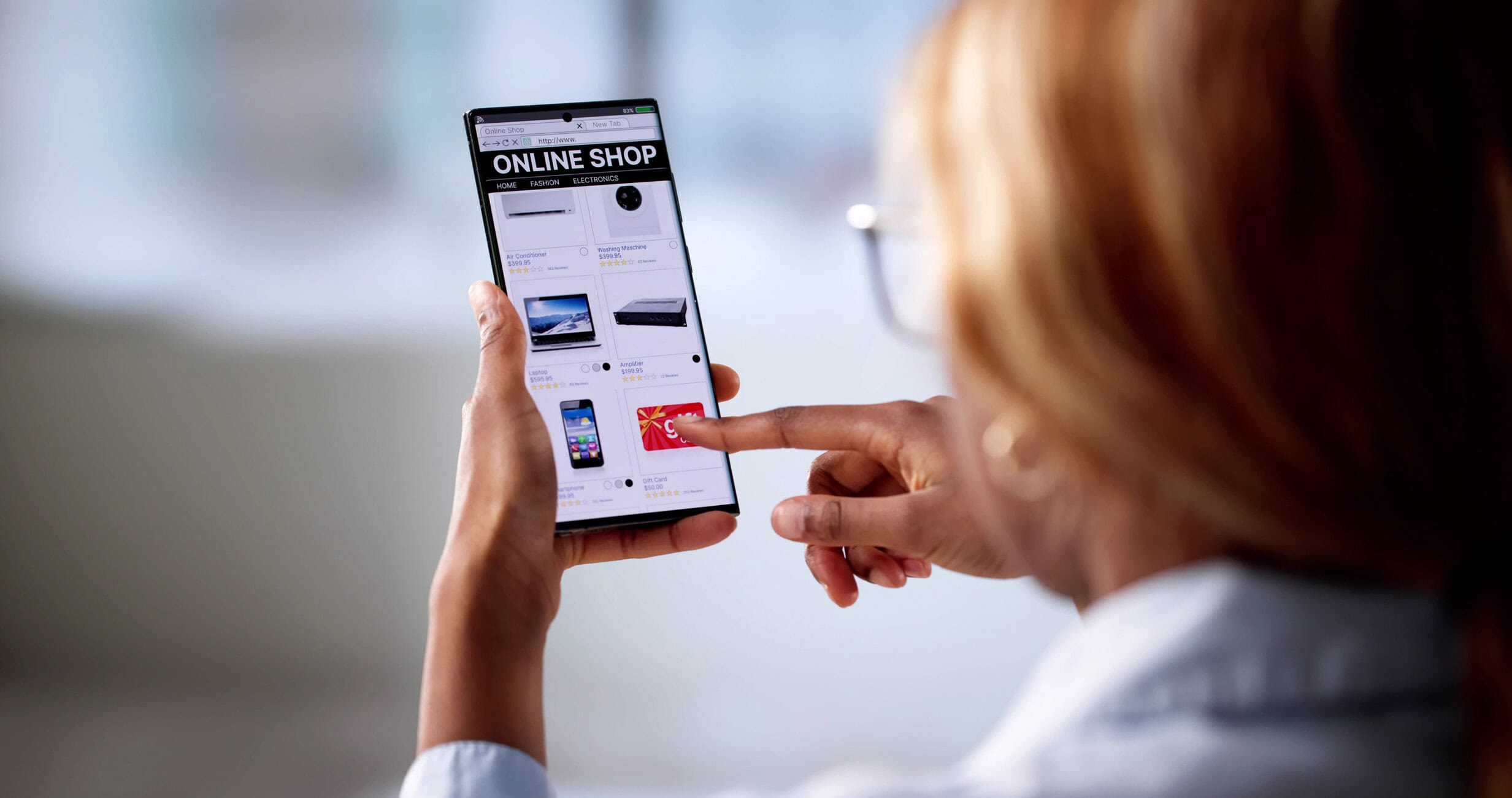 Person holding a smartphone showing an online shopping catalog with product images on the screen