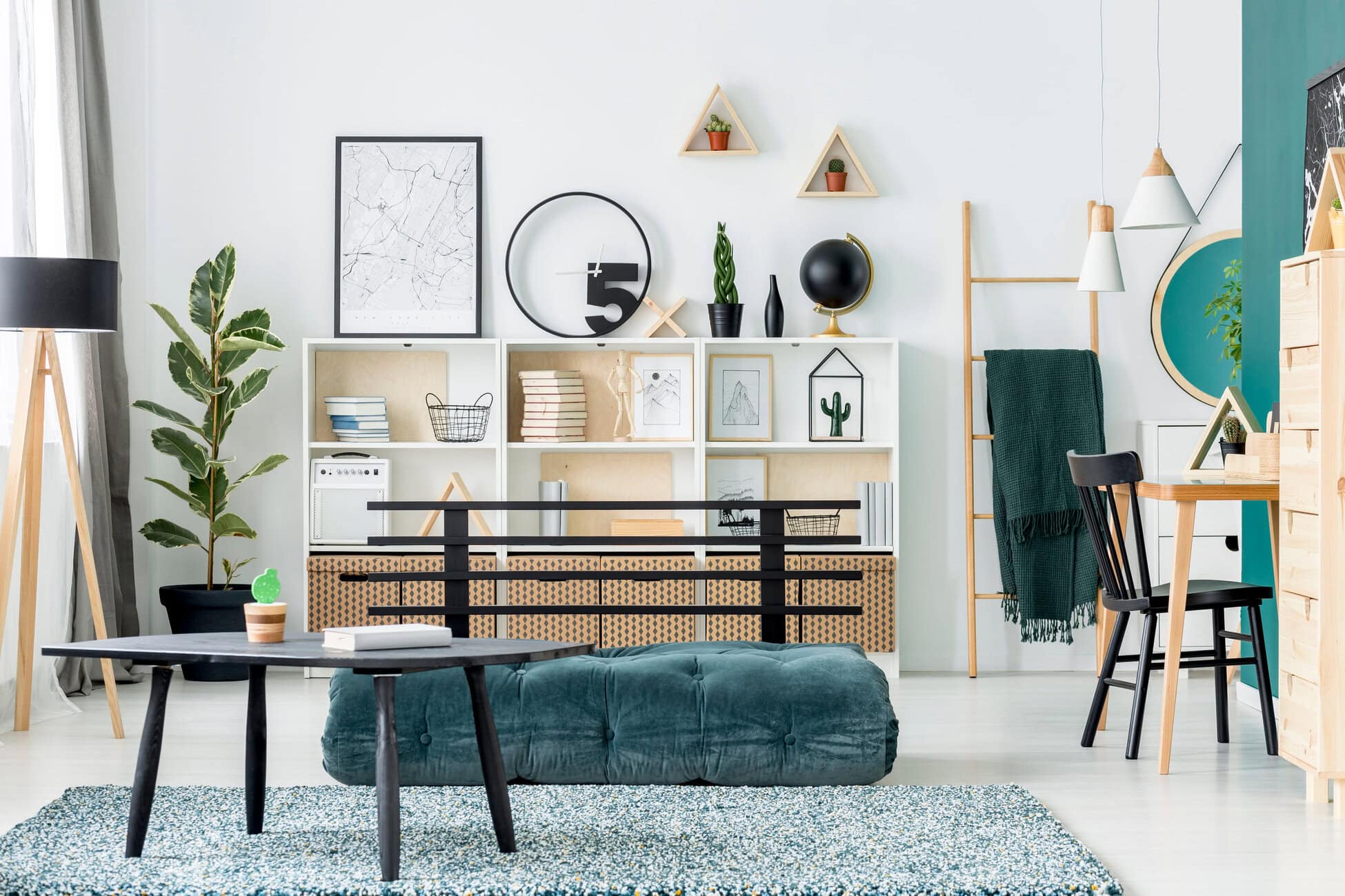 Bright modern living room with white shelving, green plants, framed art, and a dark teal sofa. Consistent natural light fills the space.