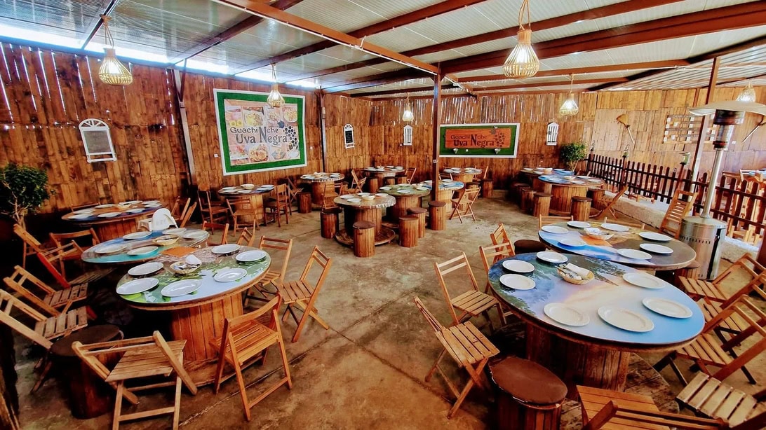 rustic open-air dining area with round log tables and wooden chairs, set for a feast with plates at each seat under warm pendant lights