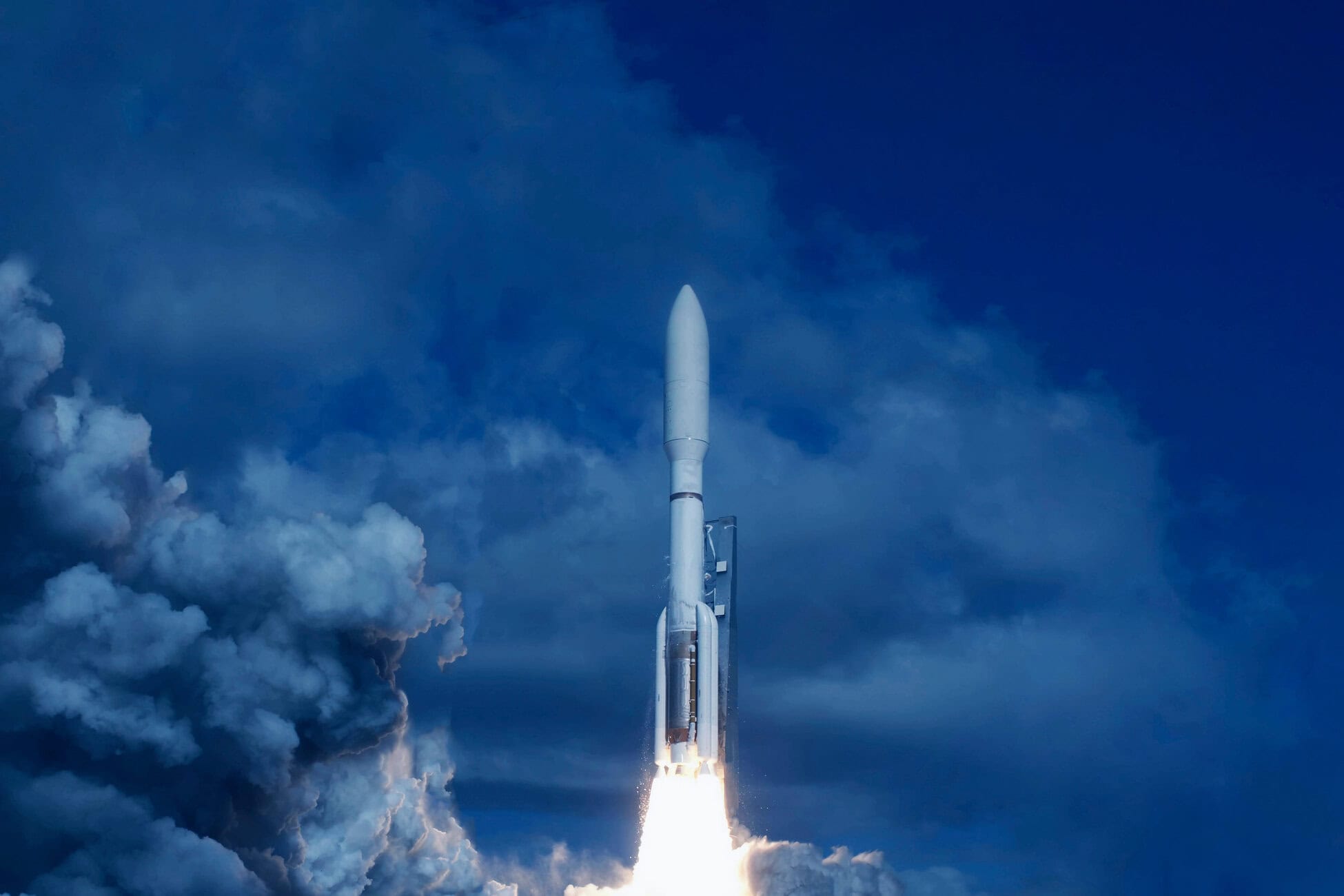 Rocket launches upward through blue sky and white clouds, bright exhaust plume at liftoff