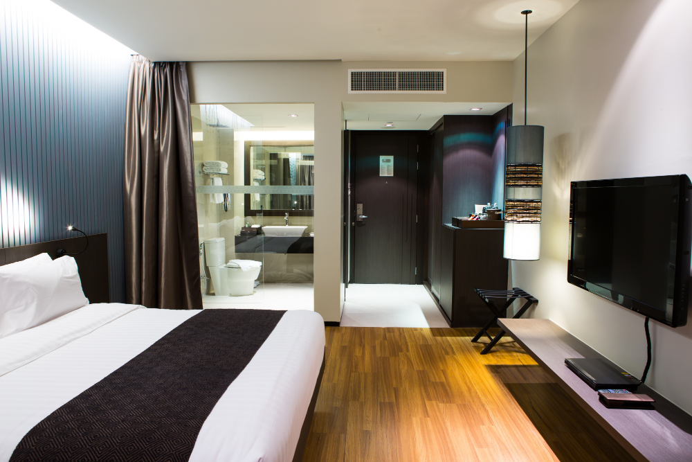 Hotel room with a king bed, blue accent wall, and a visible ensuite bathroom in the background.
