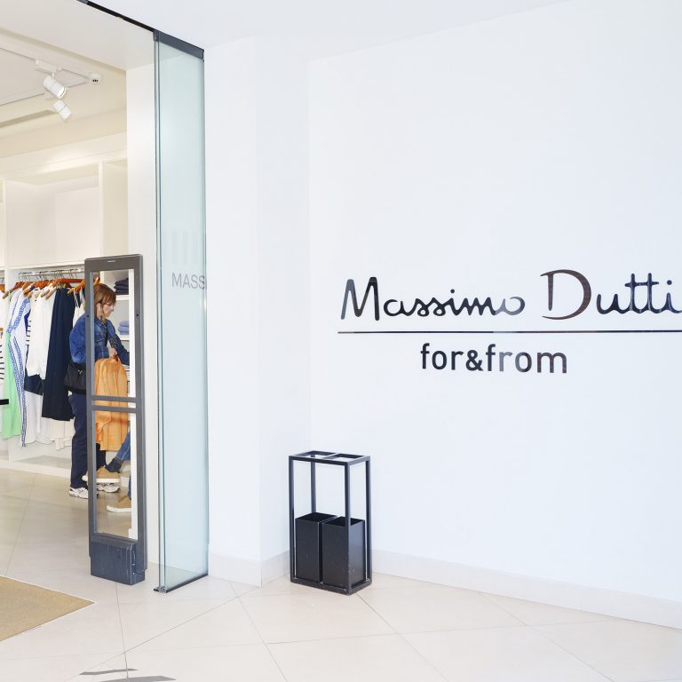 Massimo Dutti storefront interior with a glass door, white walls, and clothes on racks; logo visible on the wall: 'Massimo Dutti for&from'.