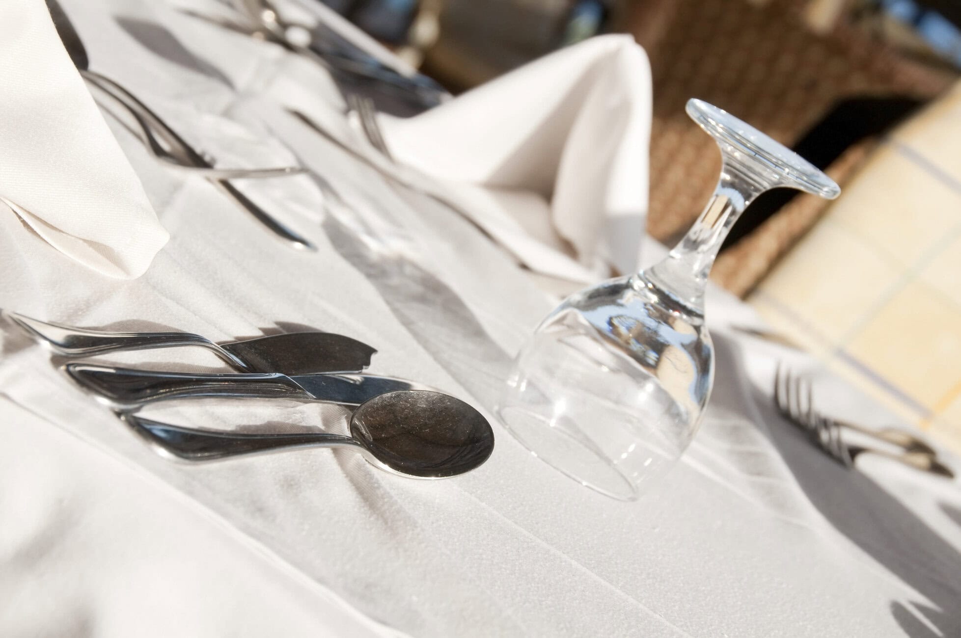 Formal table setting with polished silverware (knives, forks, spoons) arranged on a white tablecloth and a clear wine glass nearby.