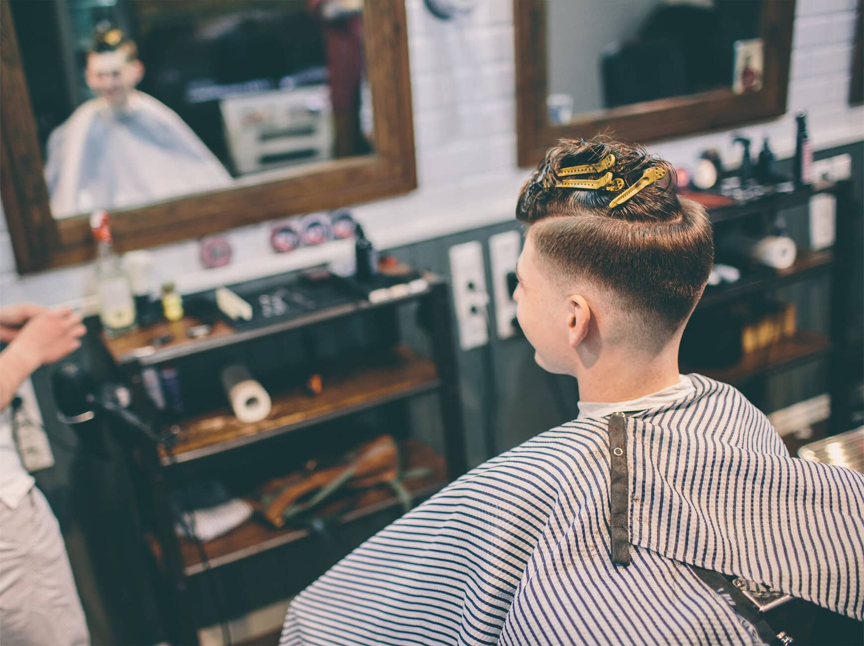Barbering in progress: back of client's head with yellow large hair clips and striped cape in a barbershop.