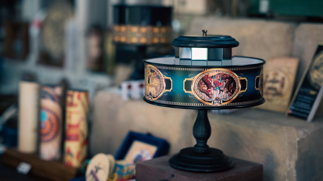 Decorative vintage lamp on a dark pedestal in a shop, featuring a teal band with gold medallions.