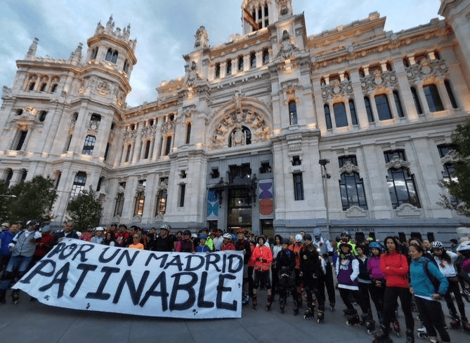 Group of people protesting with a large banner in front of a grand neoclassical building.