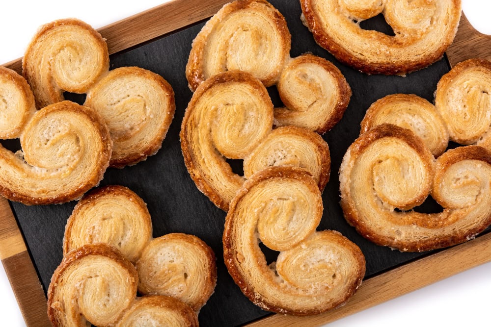 Golden palmiers pastries arranged on a wooden tray with a dark slate surface