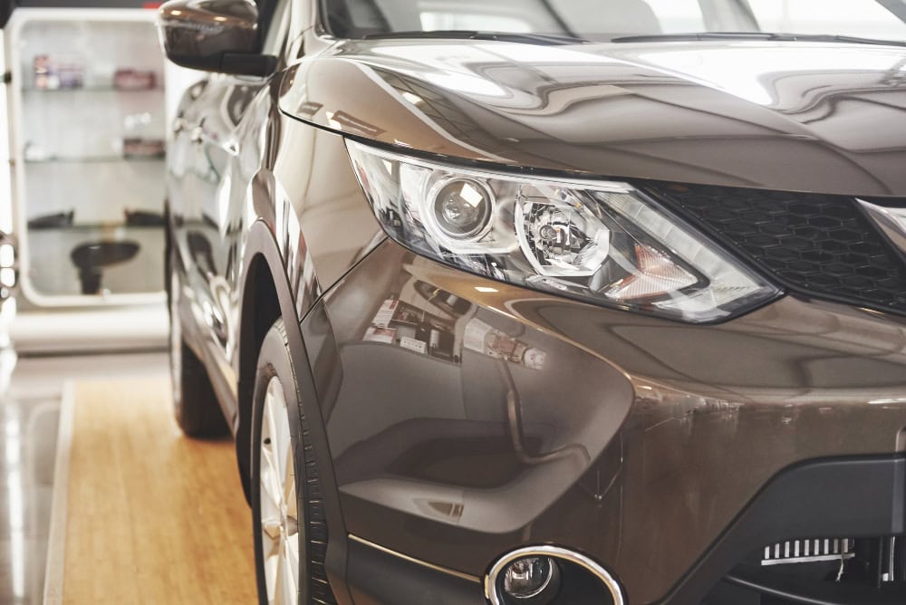Bronze SUV in a showroom, close-up of the front left side with headlight and grille visible
