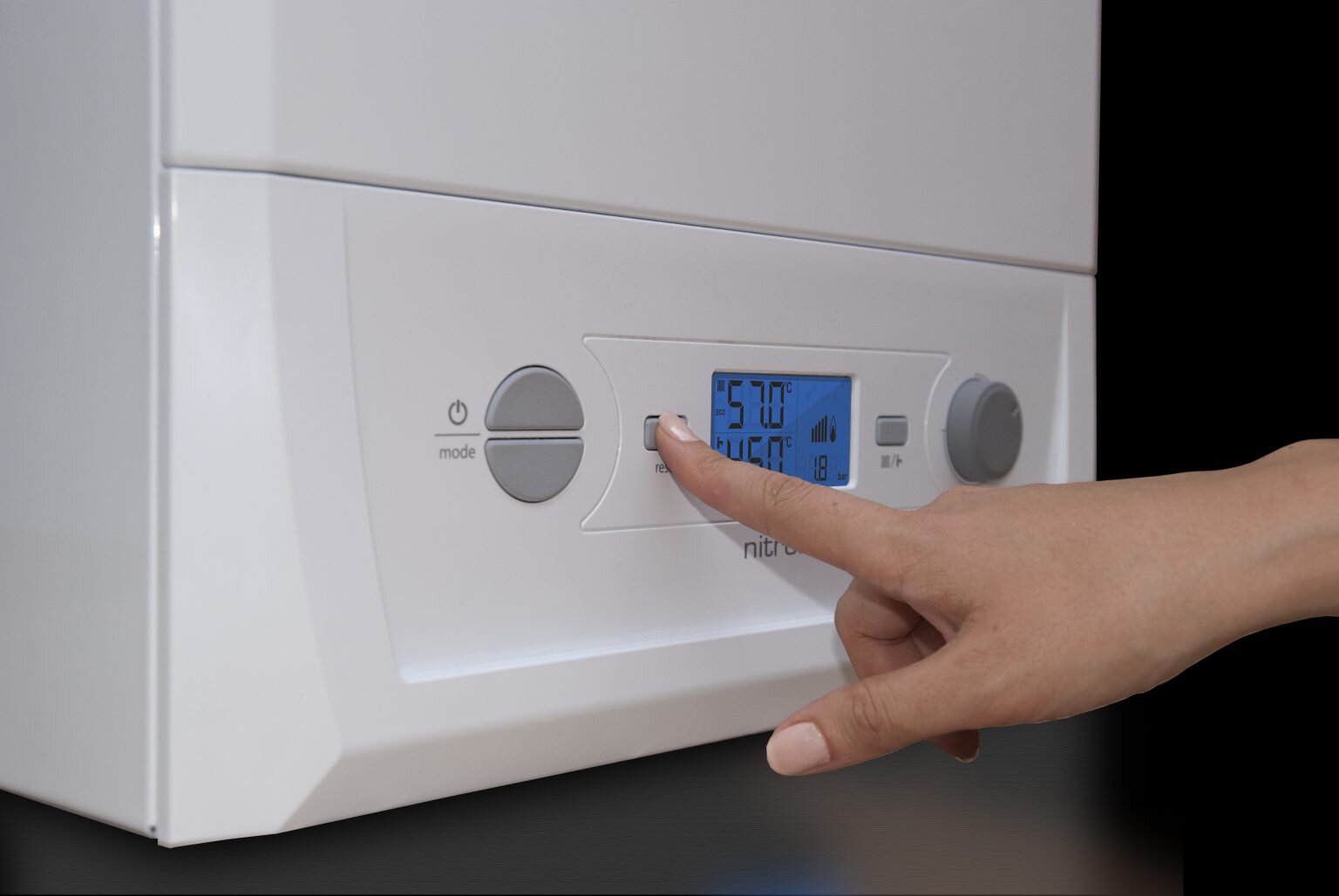 Close-up of a hand pressing a small reset/power button on a white boiler control panel with a blue digital screen showing temperature readings