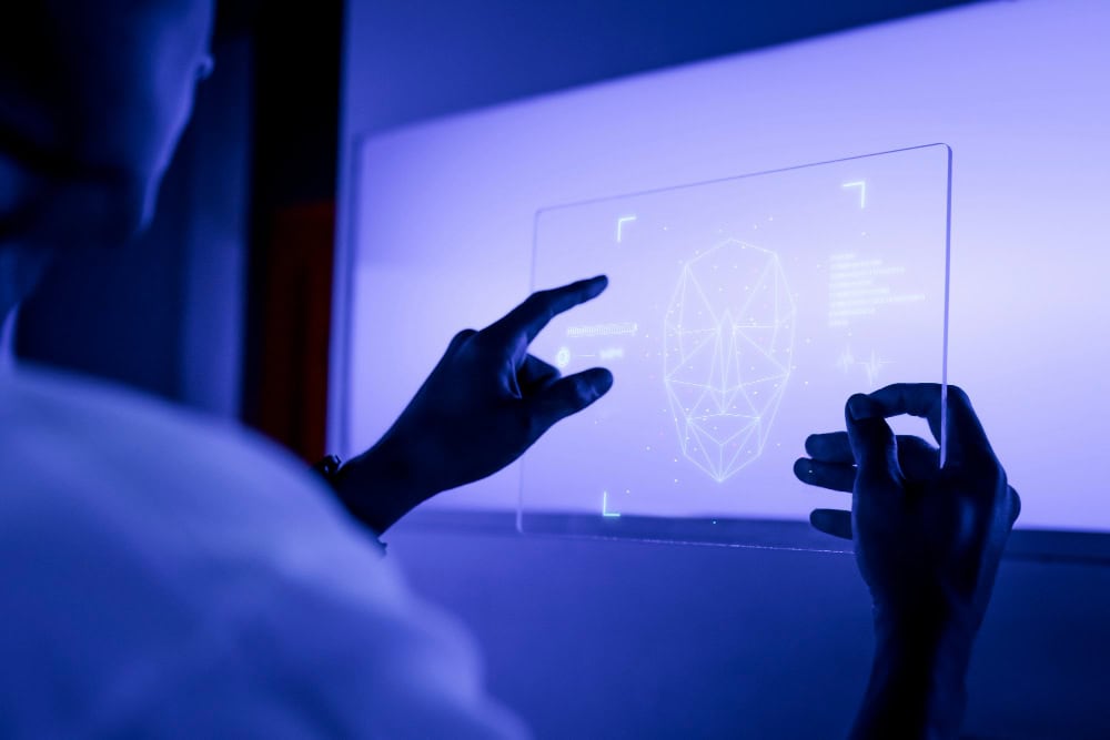 Person gestures toward a translucent holographic screen displaying a geometric head model in blue light.