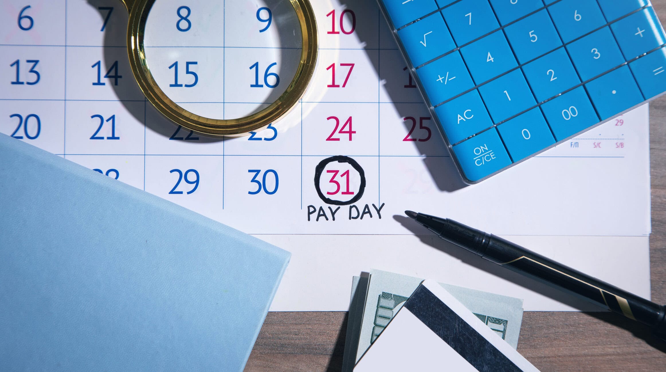 Payday marked on a calendar with the 31st circled and 'PAY DAY' handwritten nearby, with a pen and calculator in view.
