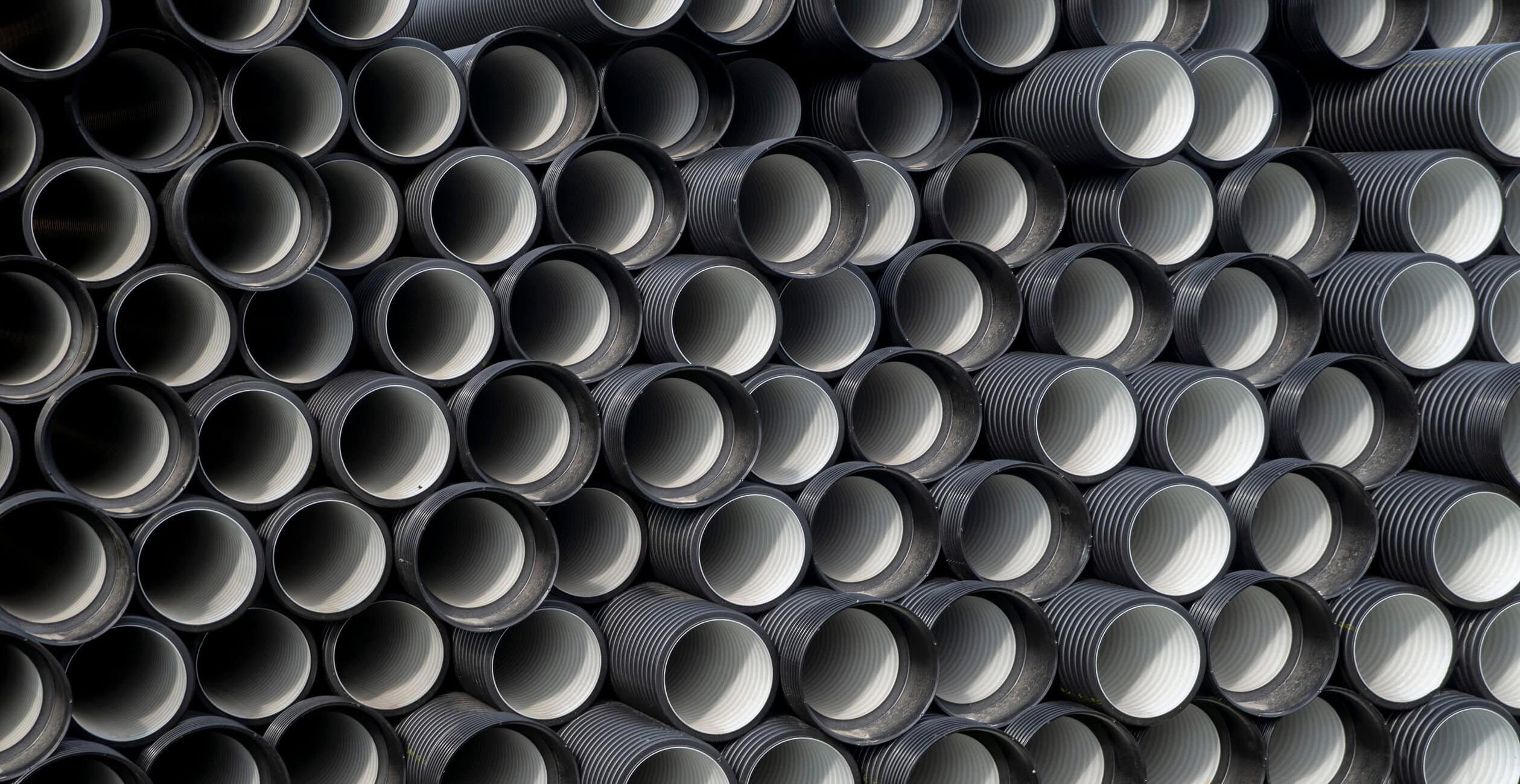 Stacked black corrugated plastic pipes viewed from the end, showing ridged interiors and circular openings.
