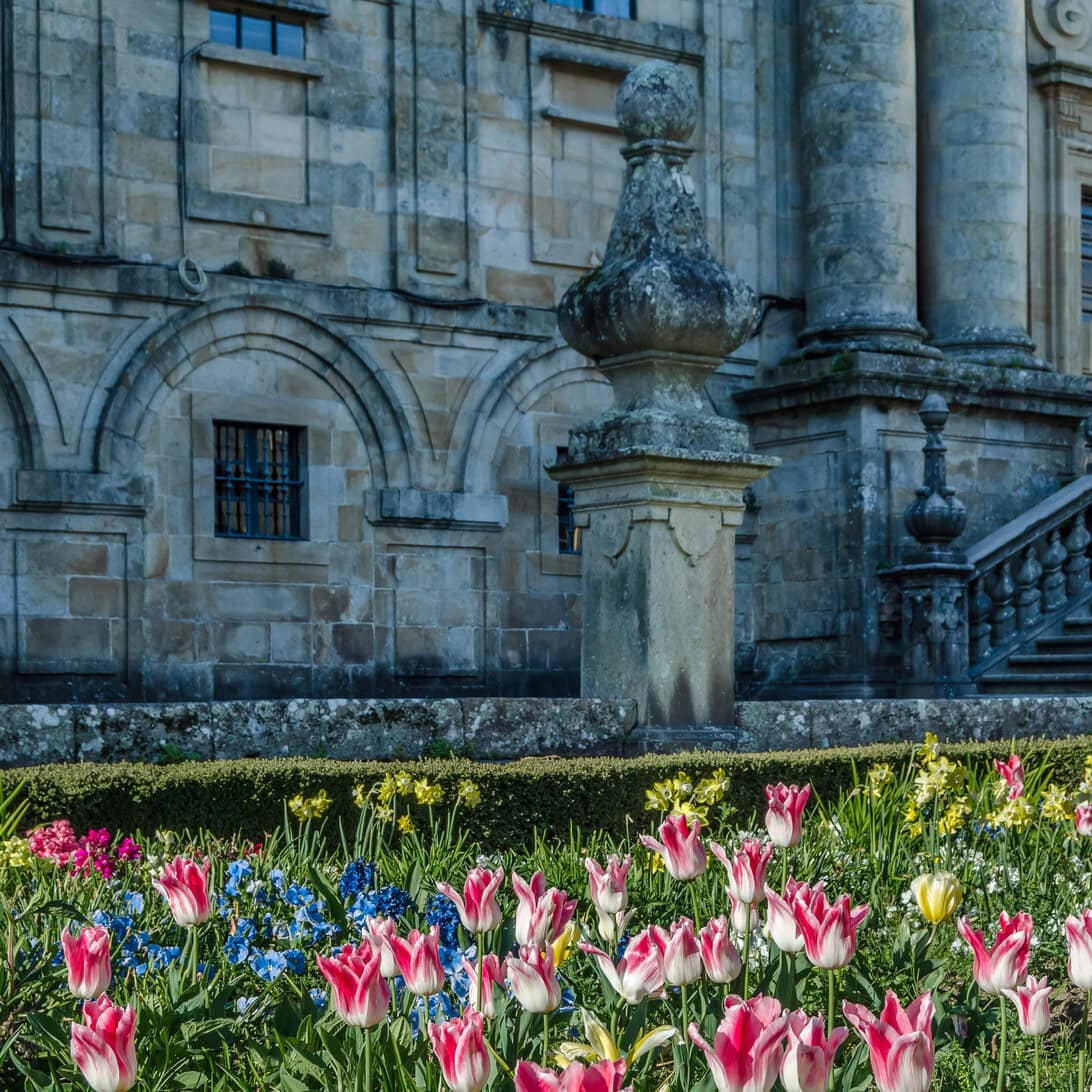 Front of a historic stone building with arched windows and a decorative urn, with a colorful tulip garden in the foreground.