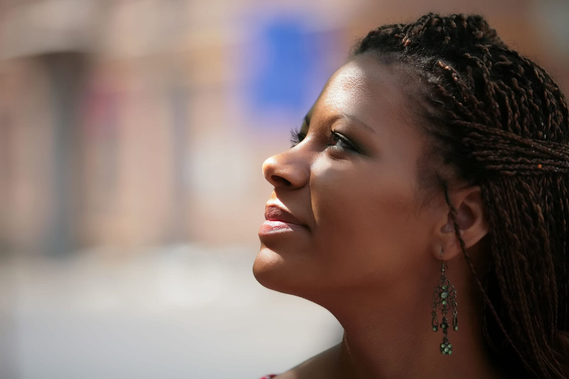 Close-up side profile of a woman with braided hair and turquoise earrings, looking upward against a blurred background.