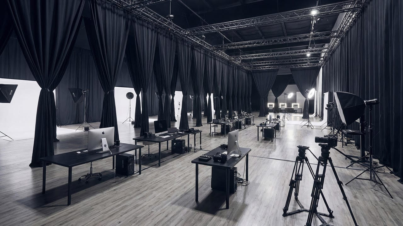 Long row of editing workstations in a professional studio, with lighting rigs and tripods nearby.