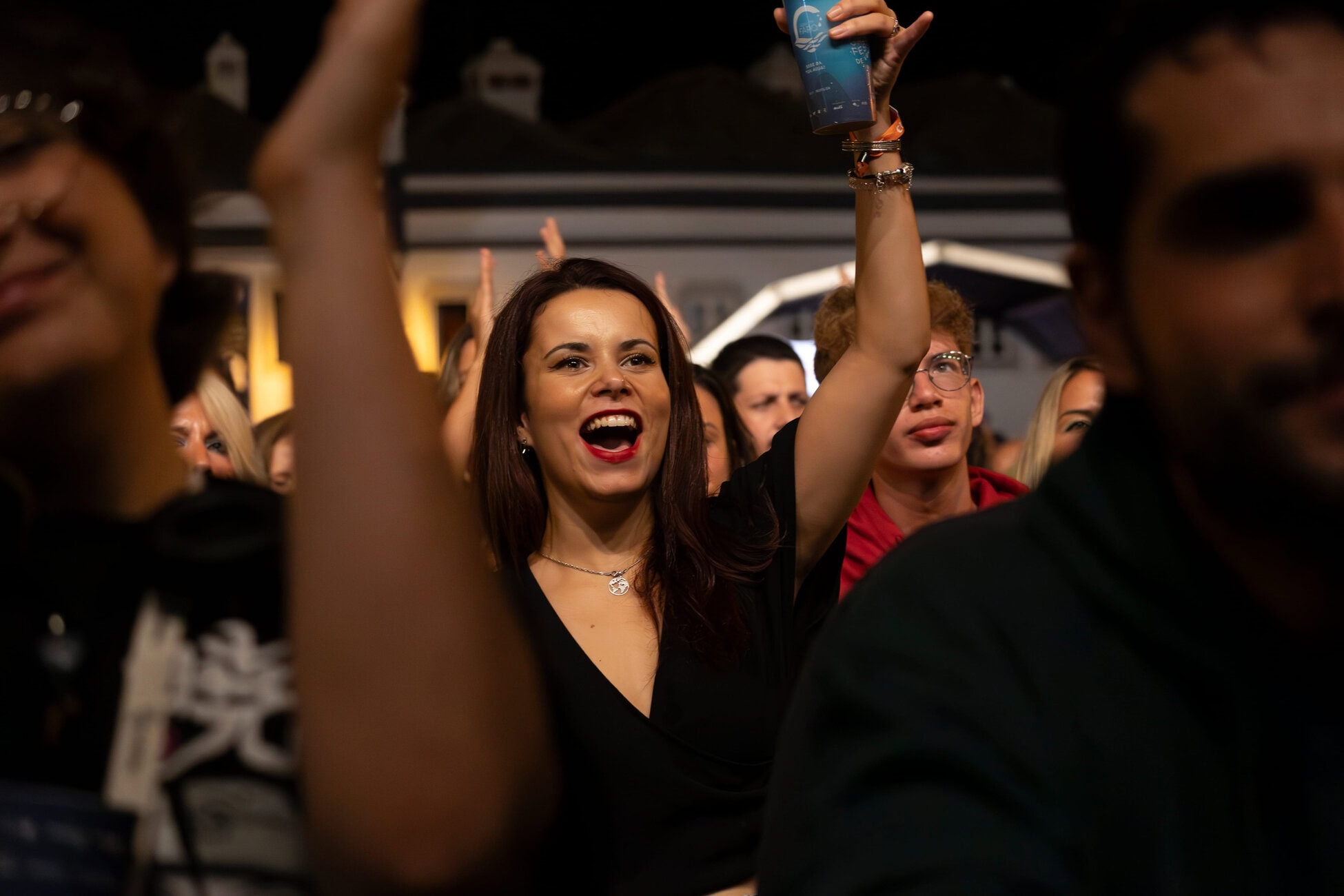 Smiling woman in black raises a blue cup at a nighttime crowd event.