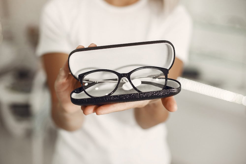 A person holding an open glasses case with black-framed eyeglasses inside, presenting them for display or storage.