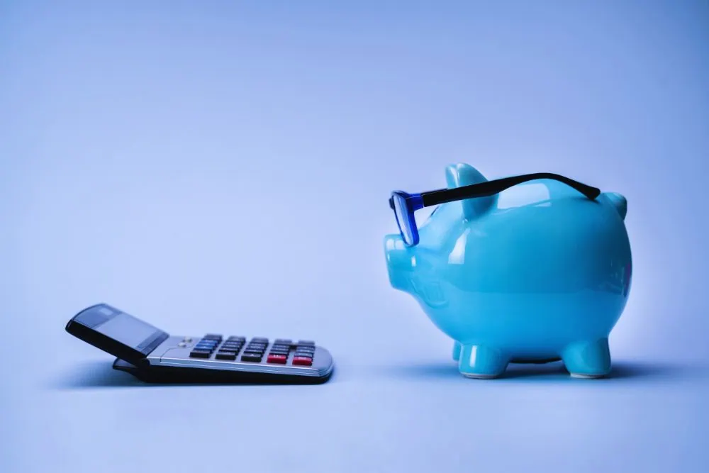 Blue piggy bank wearing glasses sits next to a calculator on a blue background, illustrating savings or budgeting for financial planning.