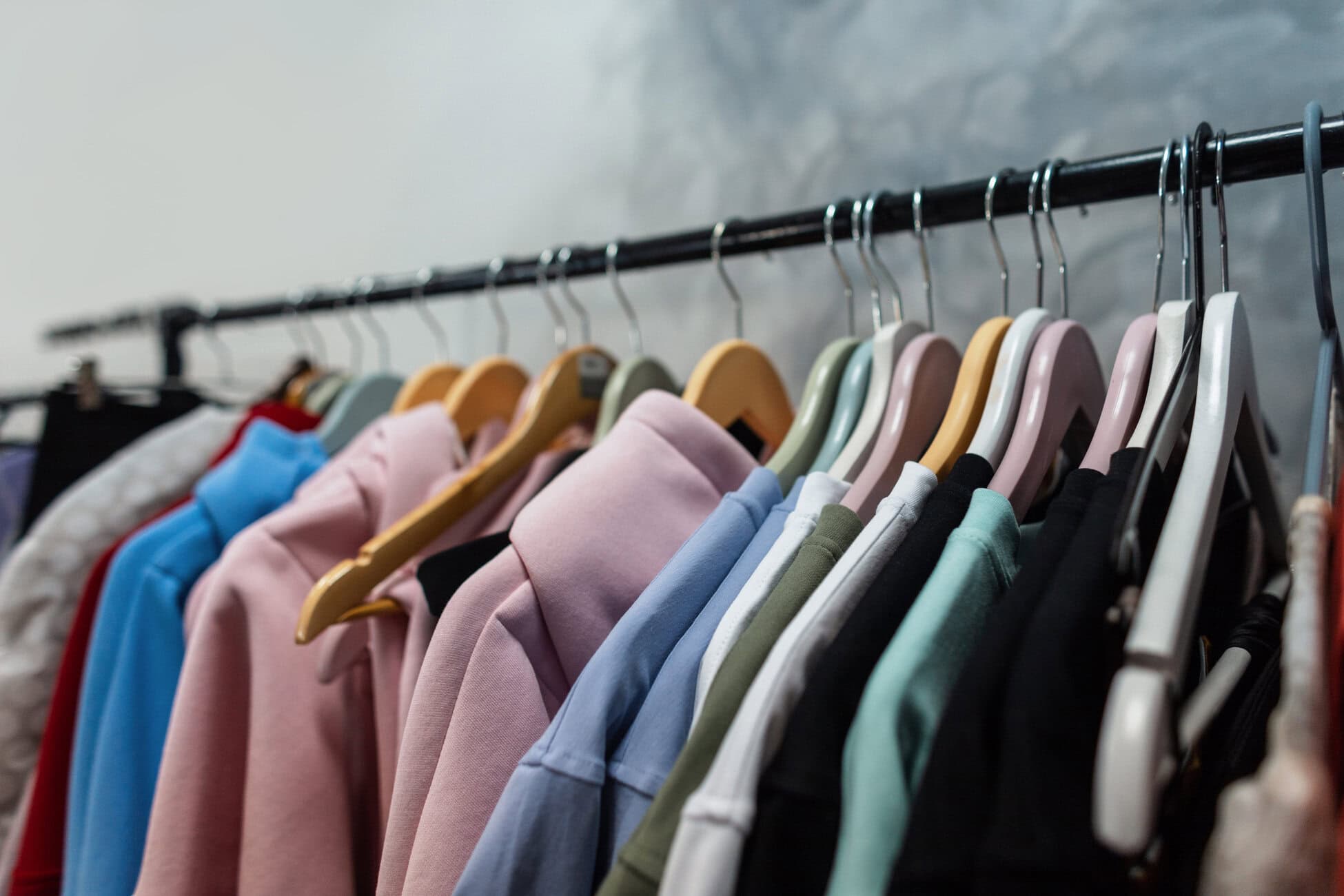 Rows of pastel-colored jackets on hangers along a metal clothing rack in a shop.