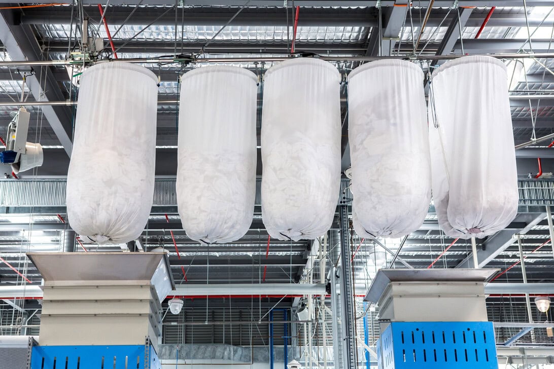 Five large white fabric filter bags hanging from a steel framework in an industrial facility.