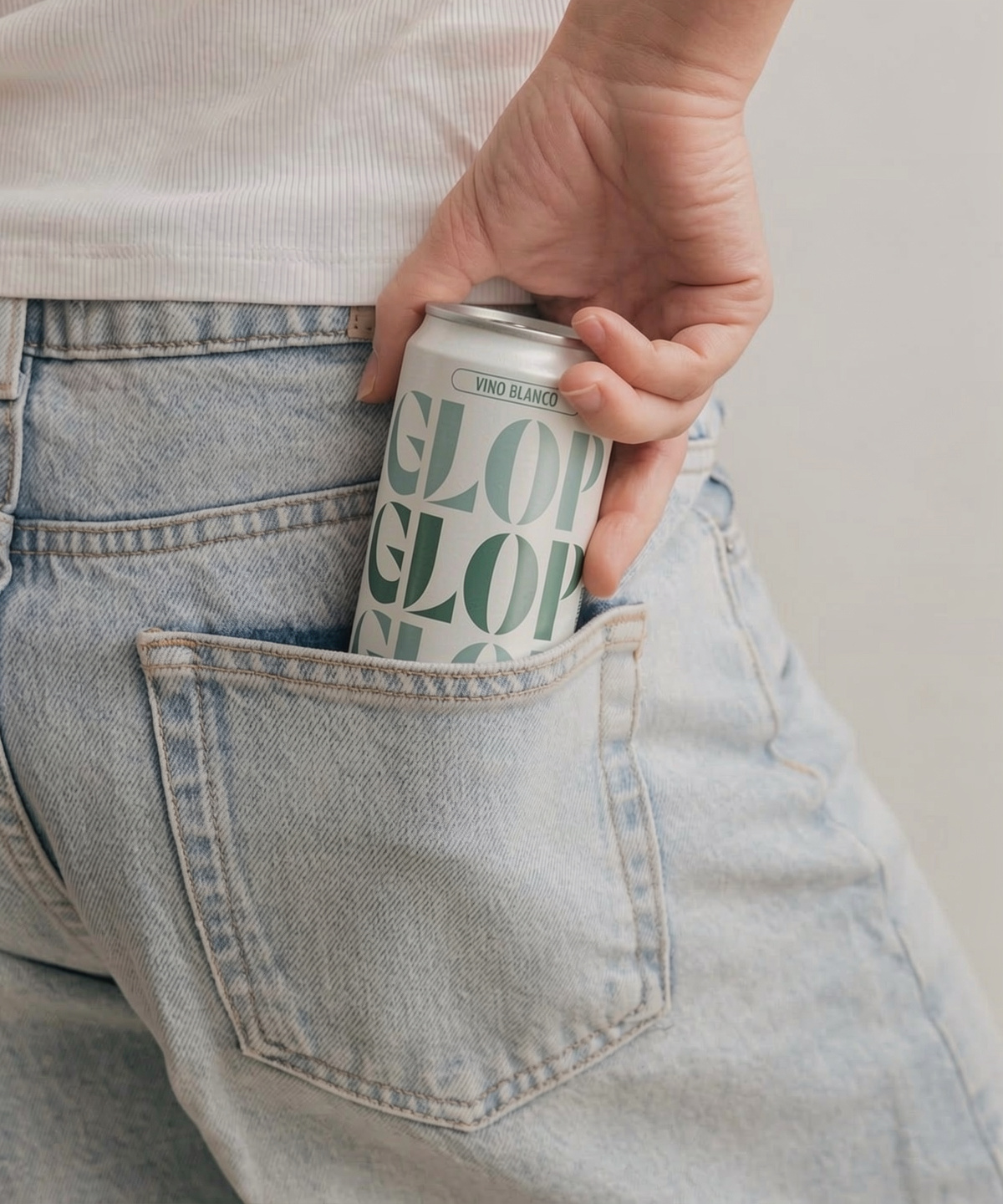 Hand placing a pale can with bold green logo into the back pocket of light-wash jeans.