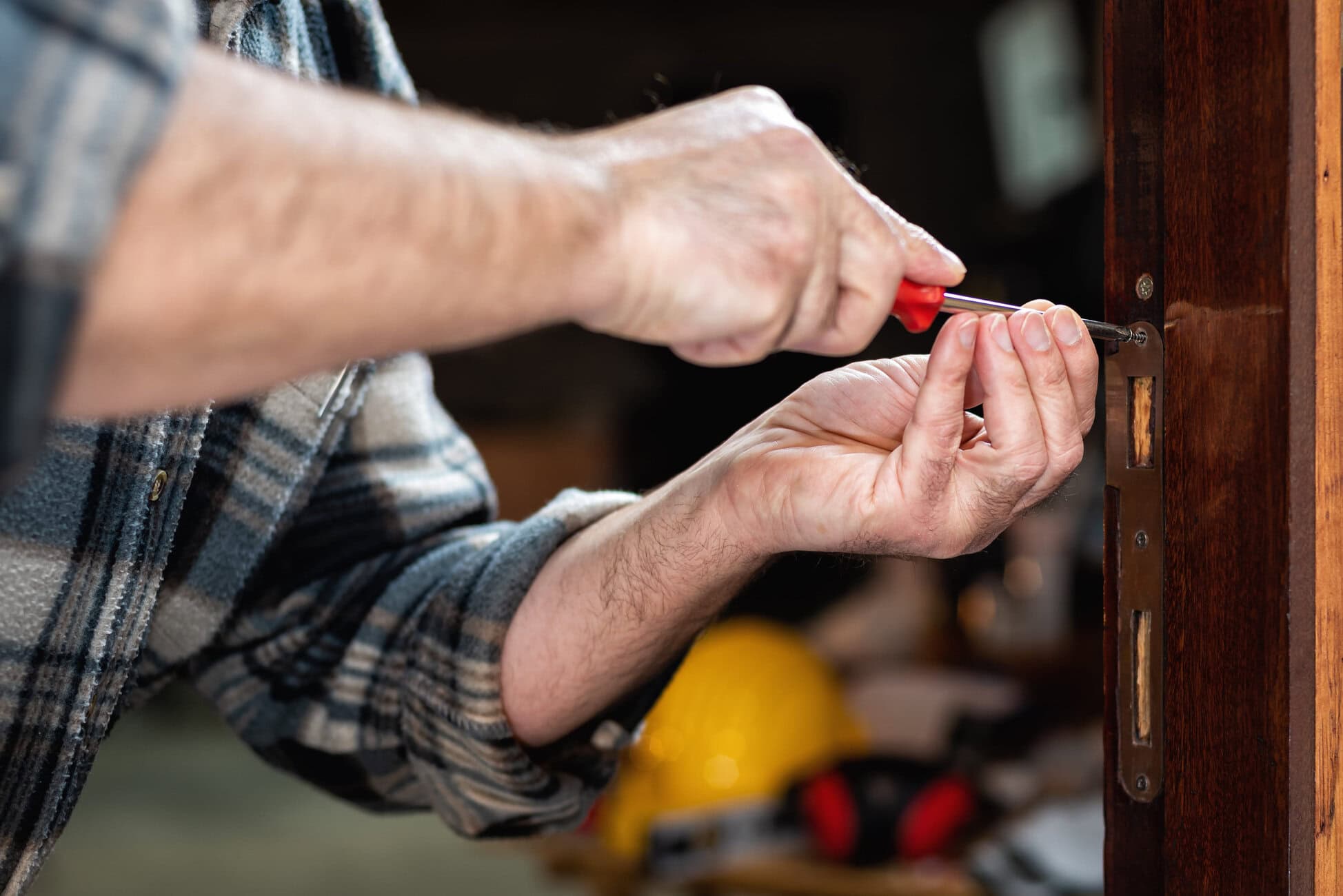 Person using a screwdriver to tighten a screw in a wooden door lock, close-up of hands and tool