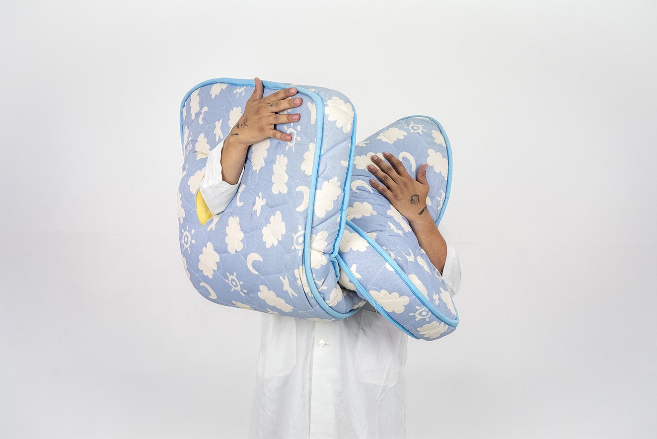 Person in a white coat holds two large blue cloud-patterned cushions stacked together against a plain background.