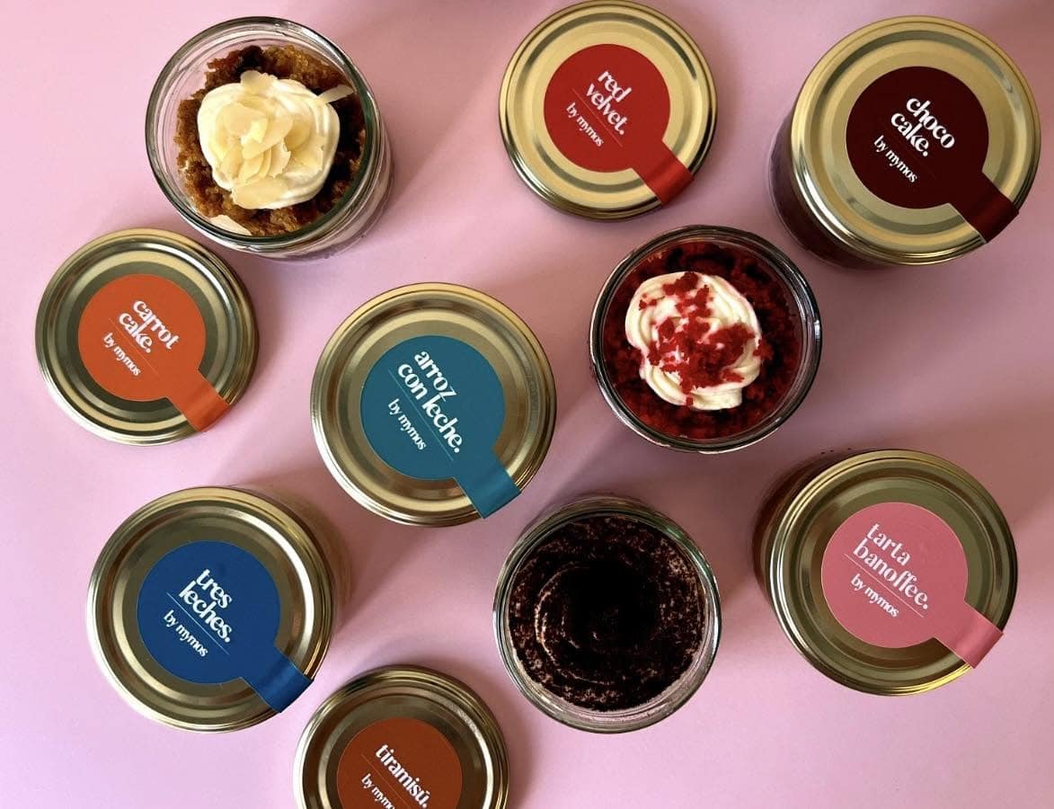 Top-down view of several dessert jars with colorful labels on a pink surface.