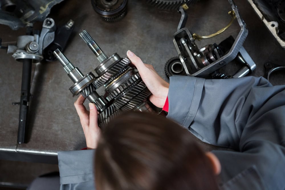 Mechanic's hands holding a multi-gear transmission assembly over a workbench in a workshop.