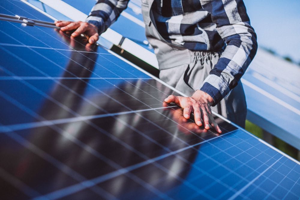 Person wearing a plaid shirt places hands on a solar panel during installation outdoors.