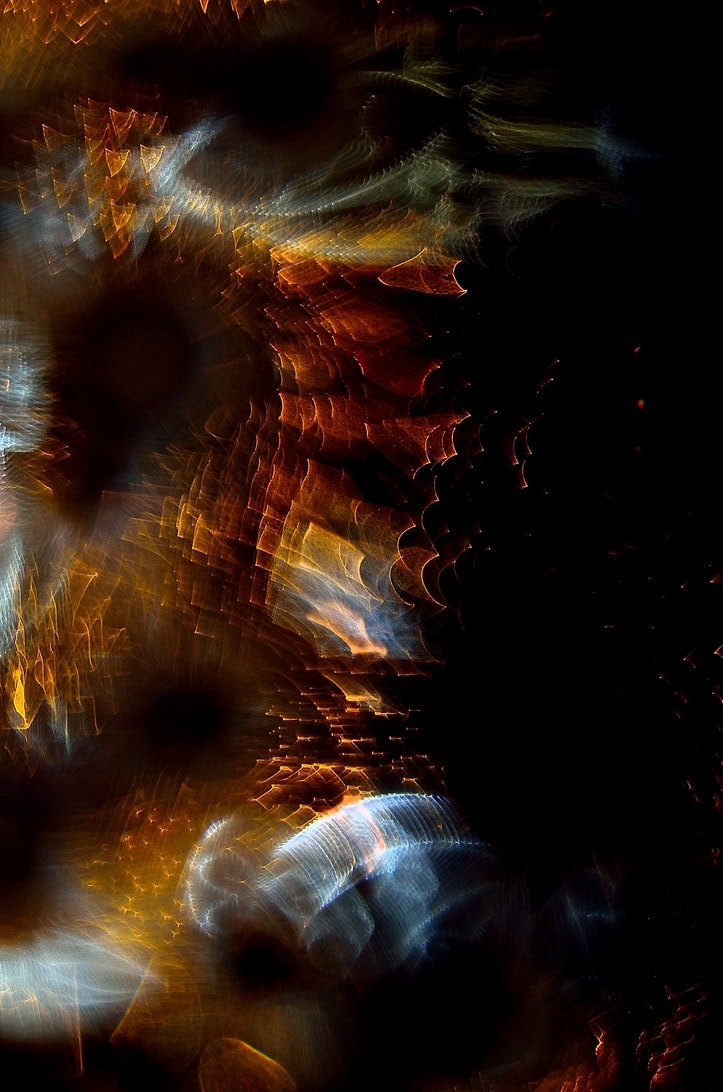 Abstract light pattern with amber, orange, and blue bokeh shapes on a dark background.