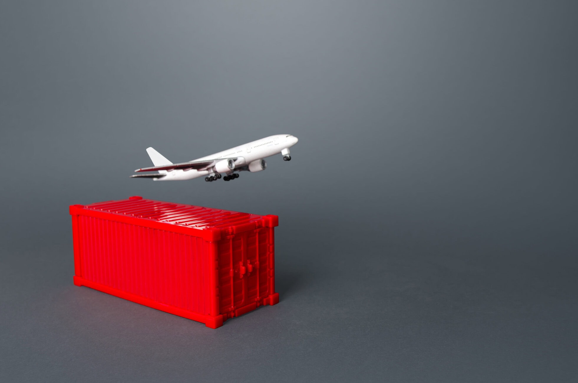 White toy airplane lifting off from the edge of a red plastic crate against a gray backdrop