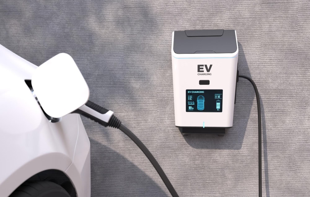 EV charging station labeled EV CHARGING with a cable plugged into a white car.