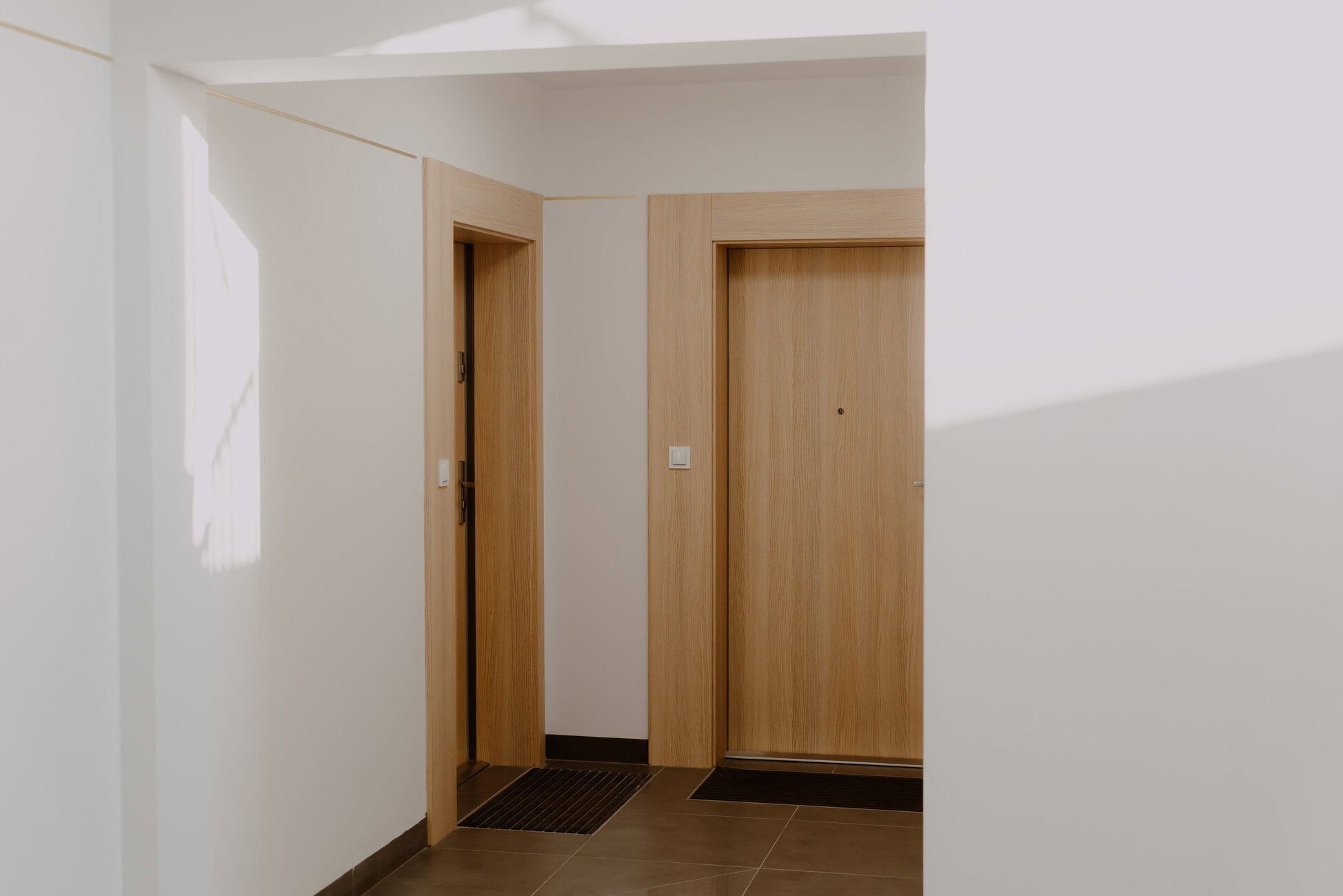 Interior hallway with open elevator doors and light wood panels on the walls, tiled floor beneath.