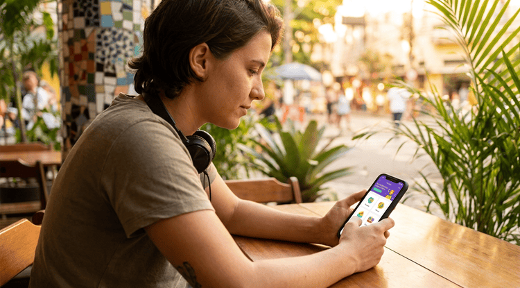 Person choosing a Brazilian Portuguese learning app on smartphone in a warm café setting, comparing language study options