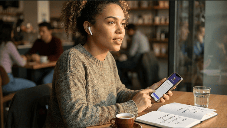 Woman practicing spoken Portuguese on a language learning app at a café, notebook with vocabulary notes beside her