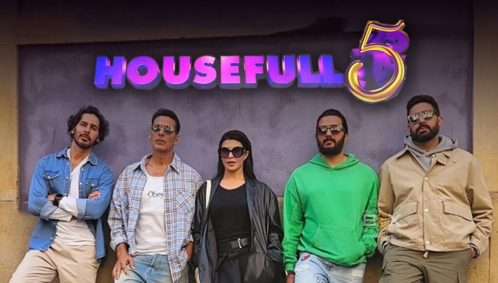 Brightly lit promotional image of the cast from the movie Housefull 5 standing in front of a signboard with the movie title, showcasing a fashionable and diverse group of actors promoting the latest Bollywood comedy film.
