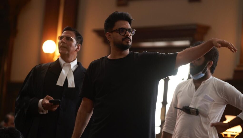 A director on film set giving instructions to actors or crew members inside a historic or vintage styled room, emphasizing behind-the-scenes of filmmaking and movie production.