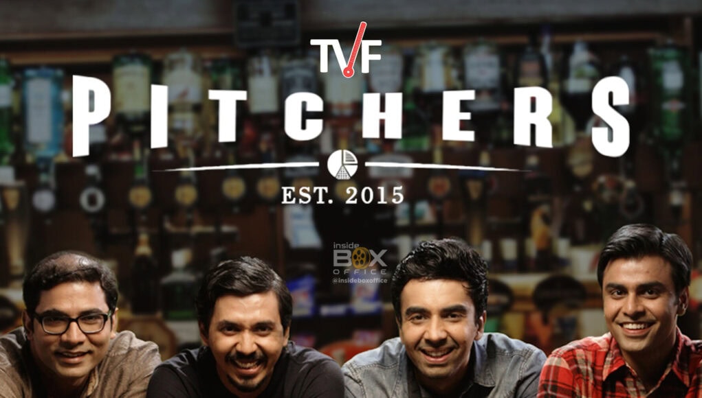 A group of four men sitting at a bar with bottles of Kingfisher beer in front of them, smiling and enjoying a social moment, with a blurred background of a liquor store.