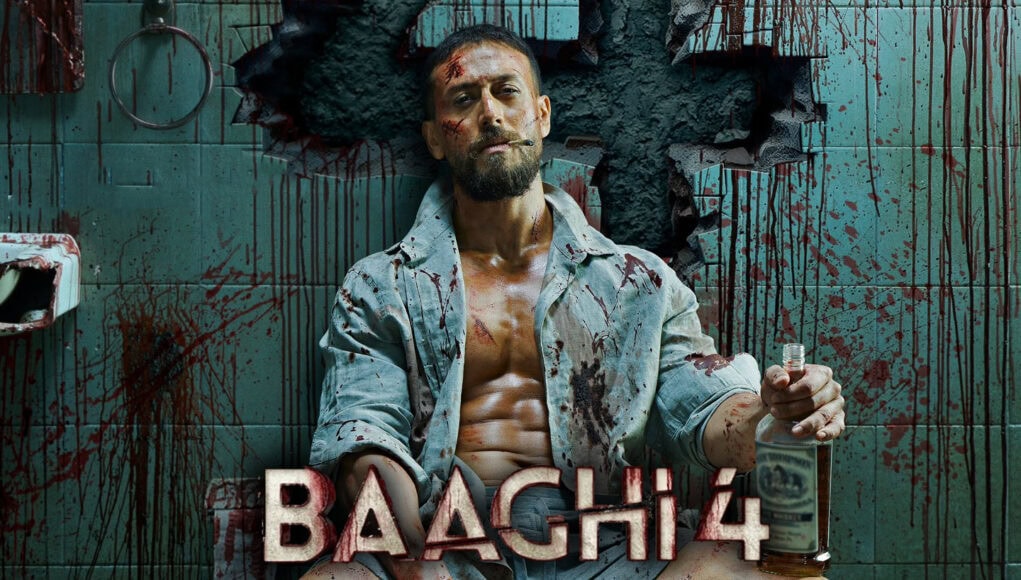 Blood-splattered man sitting on a toilet with a knife and a bottle of alcohol in a gruesome, horror-themed setting from the movie "BACH 4".