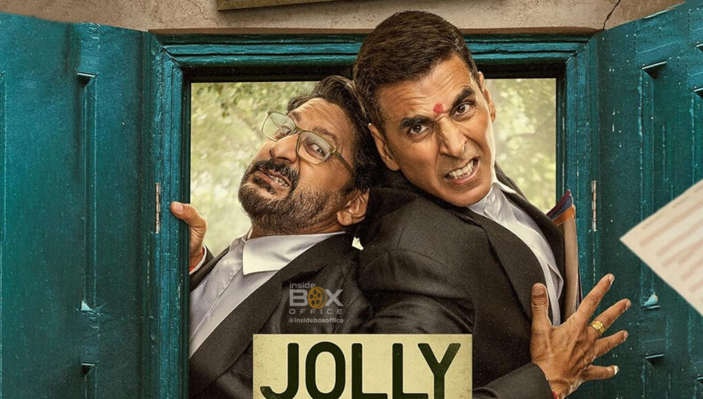 Funny Indian movie scene featuring two actors in formal suits, exaggerated expressions, and a lively setting with flying papers, showcasing humor and entertainment.