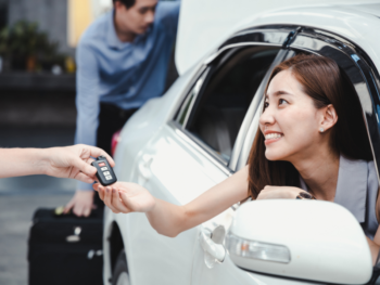 Donna sorridente seduta in auto che riceve delle chiavi per noleggio