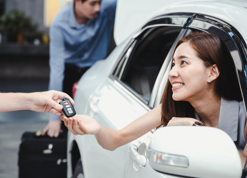 Donna sorridente seduta in auto che riceve delle chiavi per noleggio