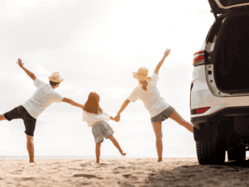Famiglia felice che corre sulla spiaggia con auto al tramonto.